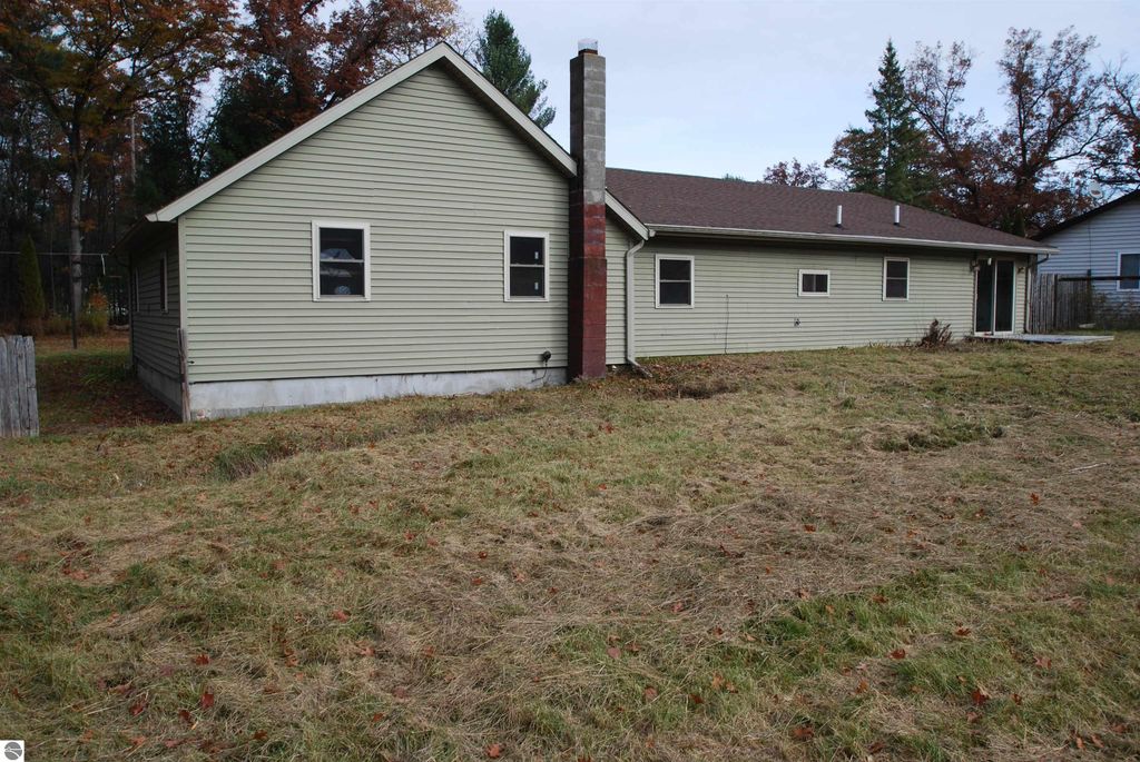 Exterior view of a fixer-upper home at 1532 Rabbit Track Drive, Alger, MI, showing a corner lot, grassy yard, and attached chimney.