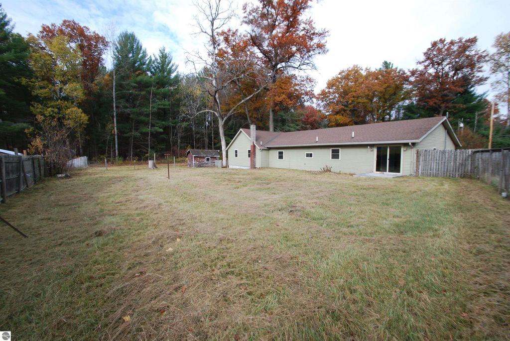Backyard view of a fixer-upper home at 1532 Rabbit Track Drive, Alger, MI, featuring a spacious grassy area, surrounded by trees and a wooden fence, with an attached garage visible on the right.