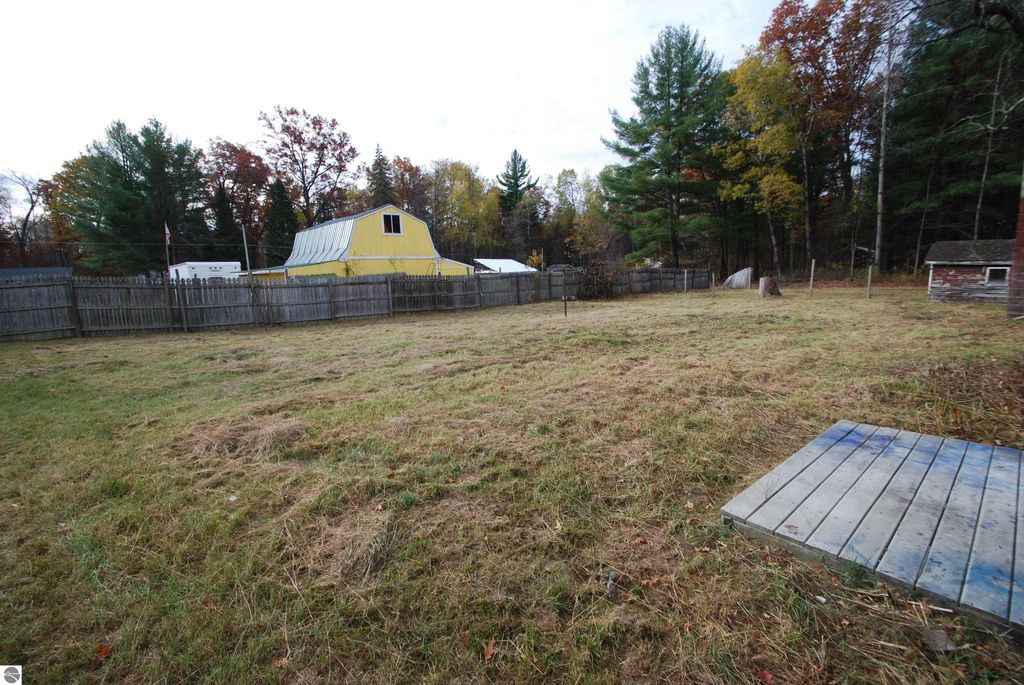 Spacious backyard of a fixer-upper home at 1532 Rabbit Track Drive, Alger, MI, featuring a wooden deck, fenced area, and surrounding trees, ideal for potential landscaping and outdoor activities.