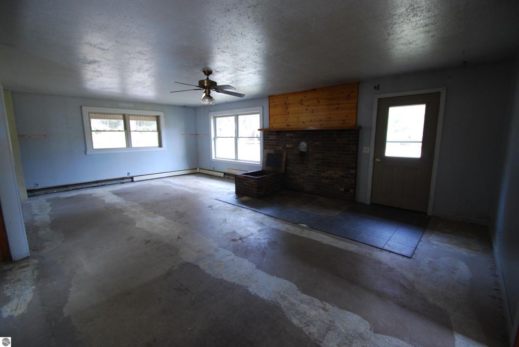 Spacious living room of a fixer-upper home at 1532 Rabbit Track Drive, featuring a ceiling fan, brick fireplace, and large windows, showcasing potential for renovation.