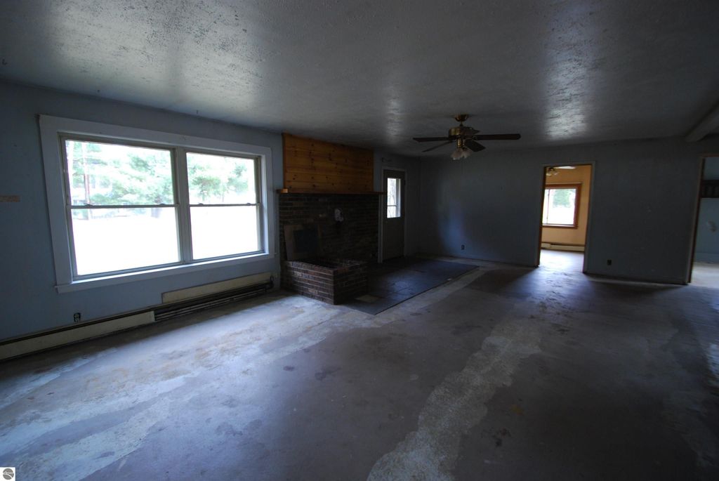 Interior view of a fixer-upper home at 1532 Rabbit Track Drive, featuring spacious living area, large windows, brick fireplace, and ceiling fan, showcasing potential for renovation.