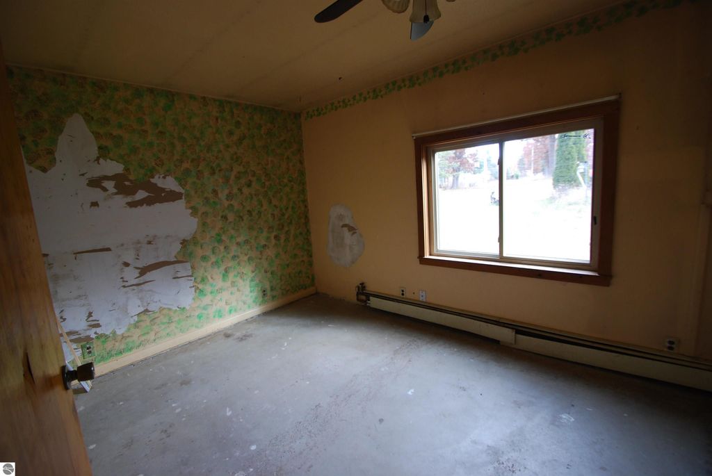 Interior view of a fixer-upper bedroom at 1532 Rabbit Track Drive, featuring unfinished walls, a window with outdoor view, and a ceiling fan, ideal for renovation potential.