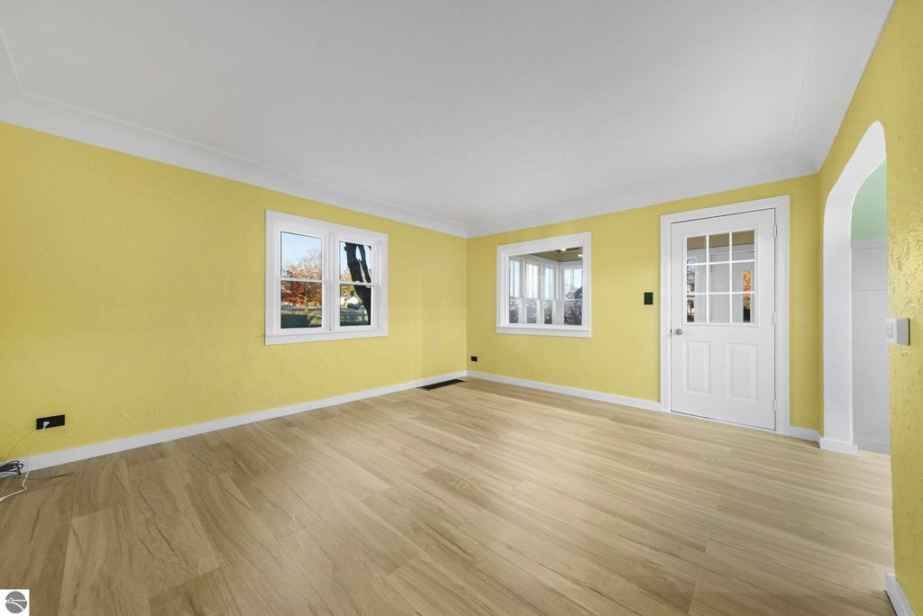 Bright yellow living room with new LVP flooring, large windows, and white door, showcasing modern updates in the McBain home at 310 E Euclid Street.