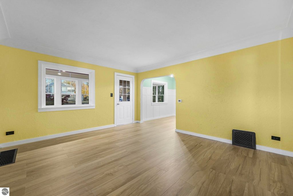 Brightly painted living room in updated McBain home, featuring yellow walls, large windows, and modern LVP flooring, showcasing a welcoming entryway.