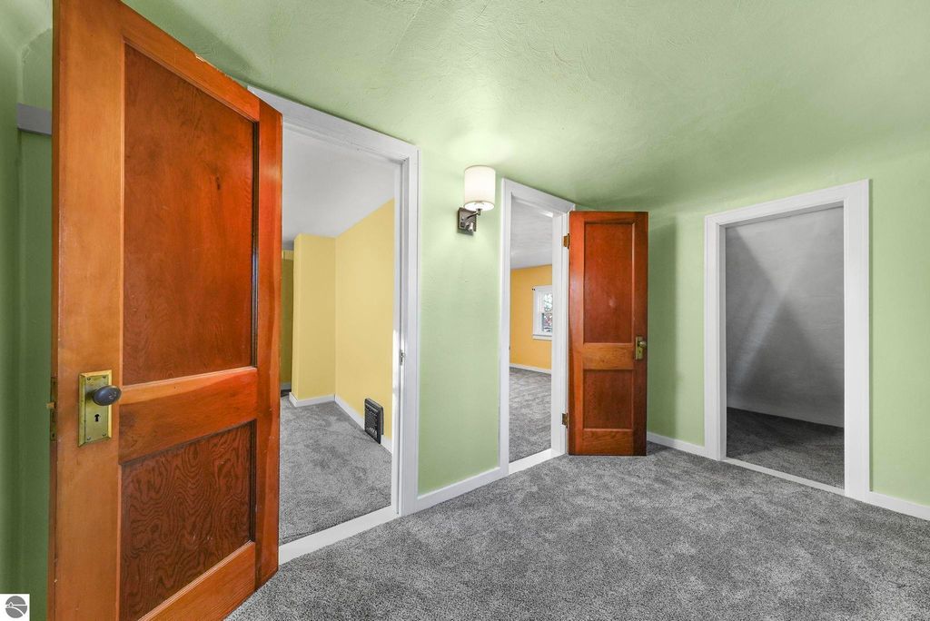 Interior view of updated home at 310 E Euclid Street, McBain, MI, showcasing green walls, new carpet, and doorways leading to bedrooms with modern lighting.