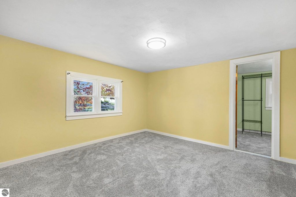 Updated bedroom with yellow walls, new carpet, and two windows providing natural light, featuring a closet and modern lighting, showcasing the interior of the home at 310 E Euclid Street, McBain, MI.