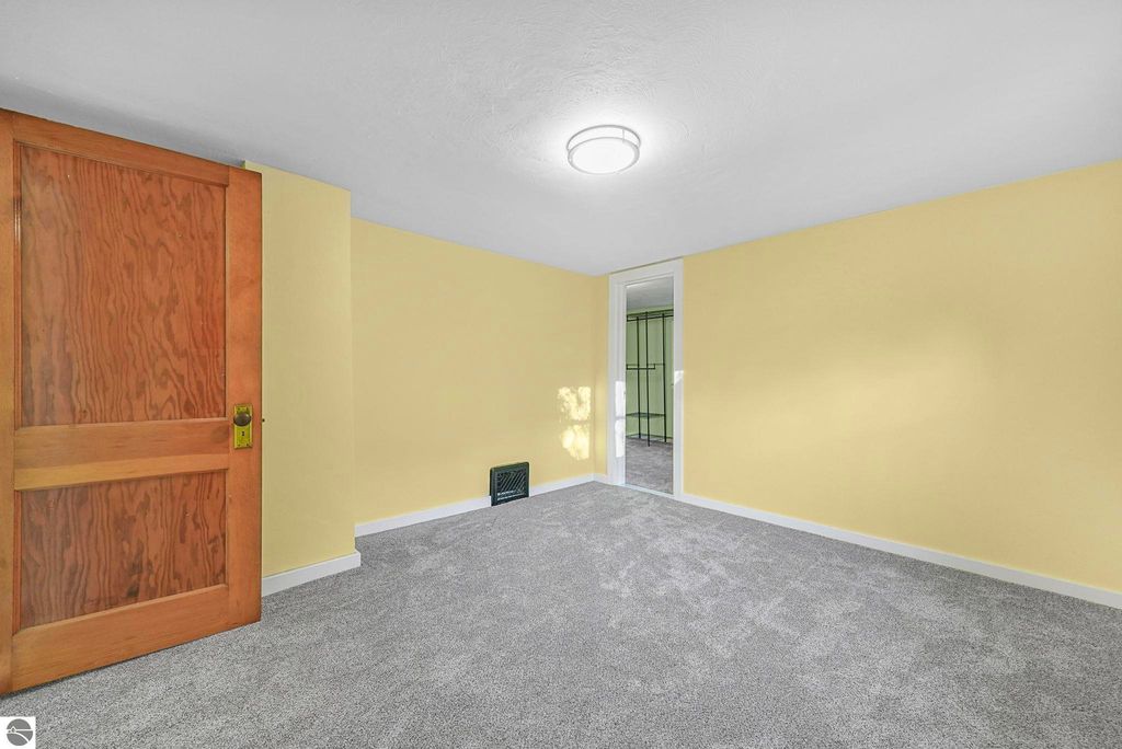 Updated interior room with yellow walls, new carpet, wooden door, and closet access, showcasing modern upgrades in a McBain home for sale.