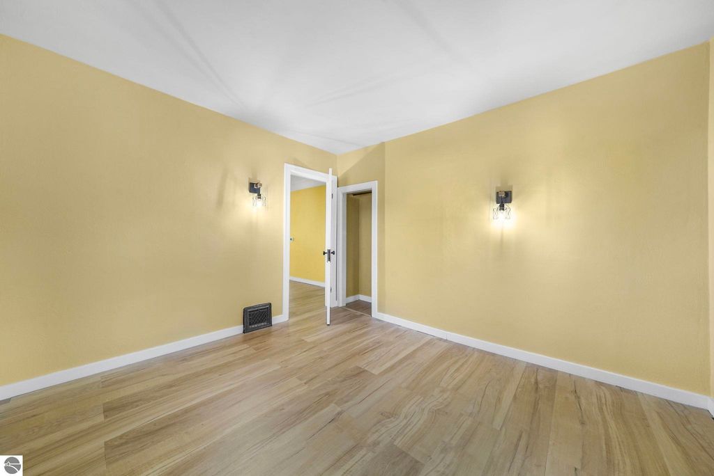 Updated interior of a residential room with yellow walls, wooden flooring, wall sconces, and an open doorway leading to another room, showcasing modern design elements relevant to the listing at 310 E Euclid Street, McBain, MI.