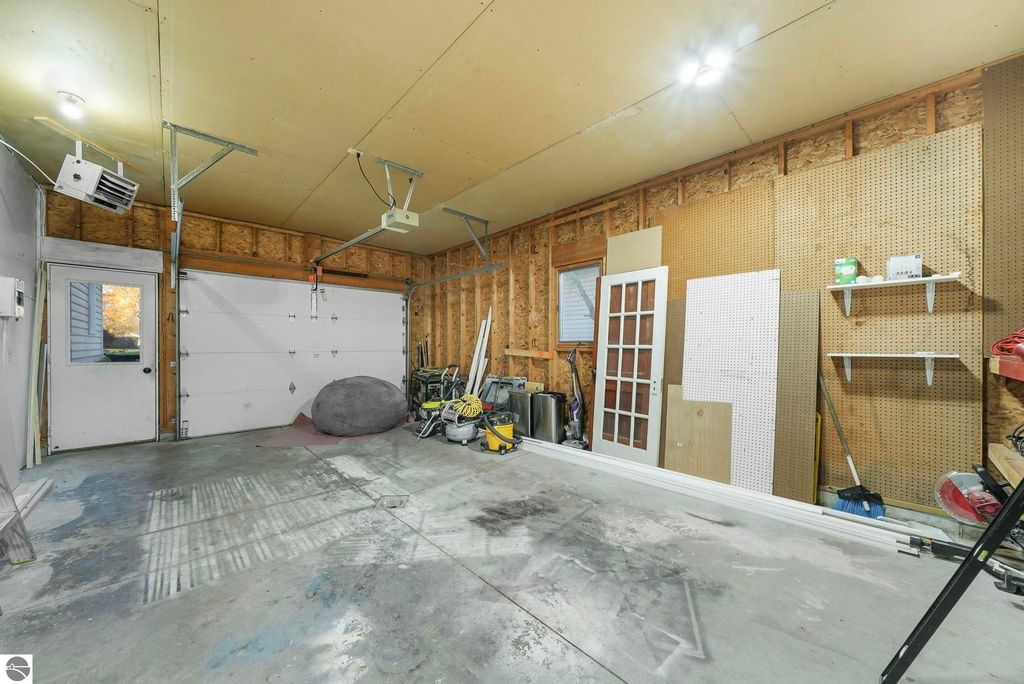 Spacious garage interior at 310 E Euclid Street, McBain, MI, featuring a large garage door, side entry door, and organized storage areas with tools and equipment.