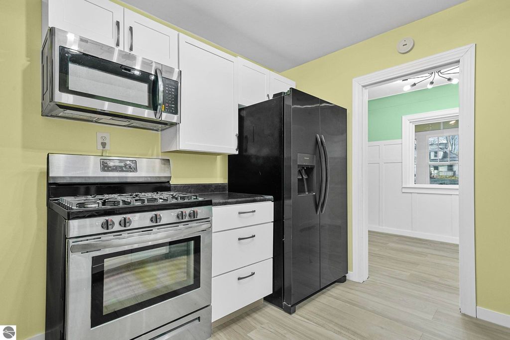 Updated kitchen featuring stainless steel appliances, including a gas stove, microwave, and black refrigerator, with white cabinets and a light yellow wall, showcasing modern design elements in a McBain home.