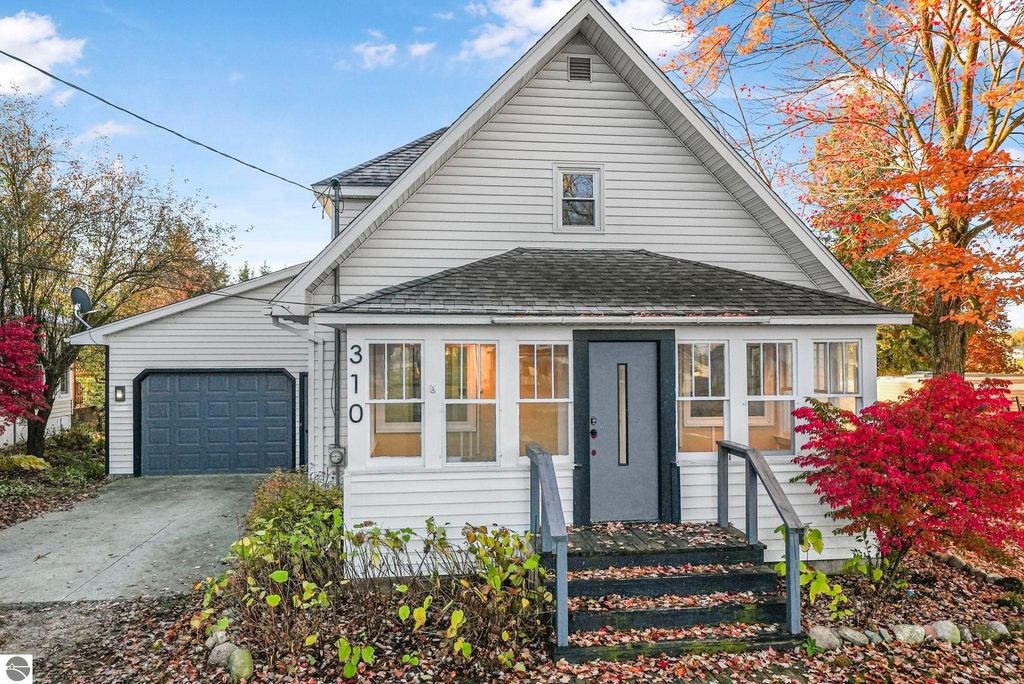 Updated exterior of 310 E Euclid Street, McBain, MI, featuring a welcoming front porch, modern entrance door, and vibrant landscaping with autumn foliage.