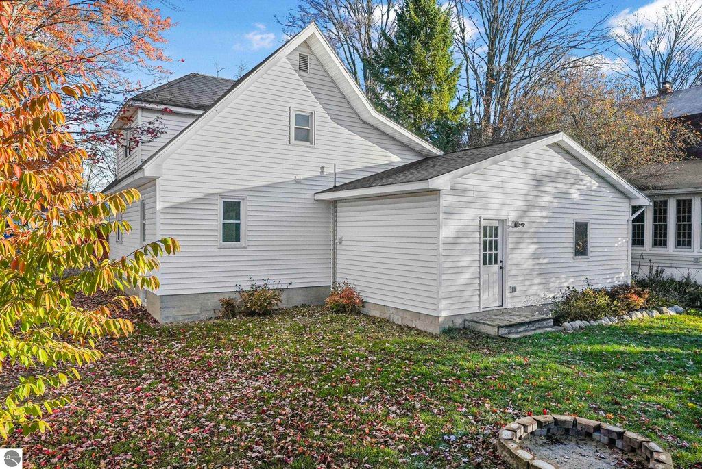 Updated white home exterior with landscaped backyard, featuring autumn foliage and a fire pit area, located at 310 E Euclid Street, McBain, MI.