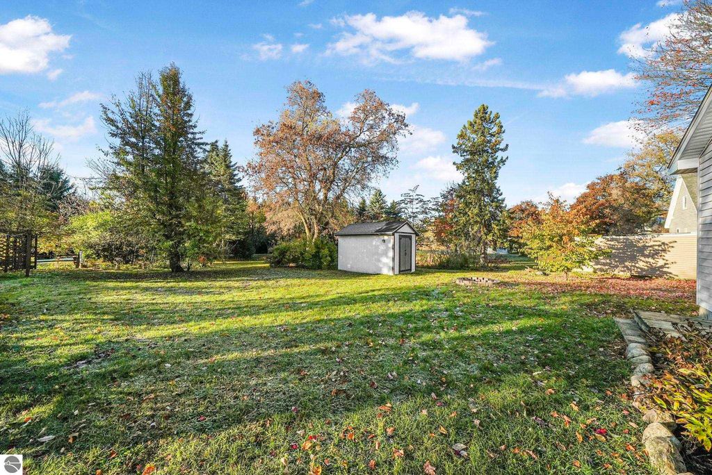 Backyard view of 310 E Euclid Street, McBain, MI, featuring a well-maintained lawn, garden shed, and surrounding trees, ideal for outdoor relaxation and entertaining.