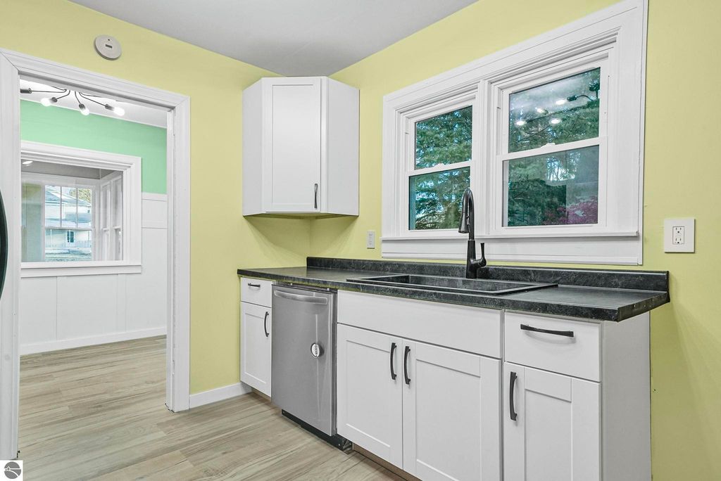 Updated kitchen with modern cabinetry, stainless steel dishwasher, and dual windows, featuring yellow walls and a stylish black countertop, in a home at 310 E Euclid Street, McBain, MI.