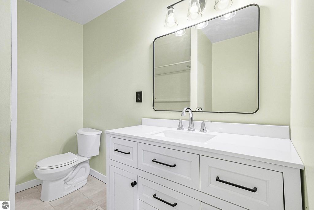 Updated bathroom featuring a modern white vanity with black hardware, a large mirror, and a toilet against a light green wall, showcasing contemporary design elements in a residential home.