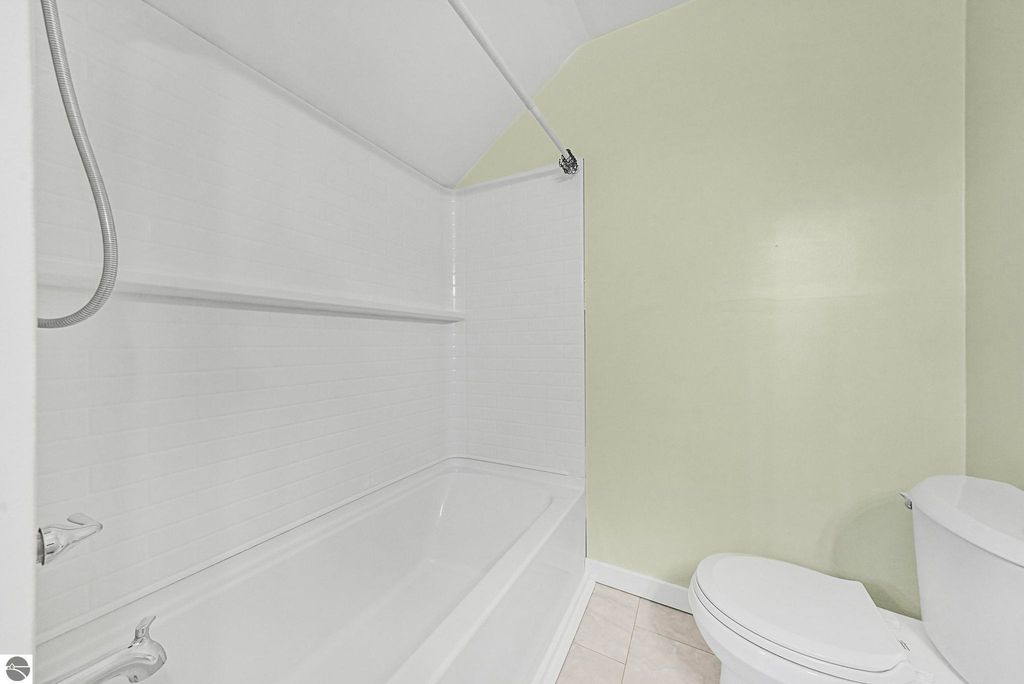 Updated bathroom featuring a white tub and shower combination, modern fixtures, and light green walls, showcasing the property's recent renovations at 310 E Euclid Street, McBain, MI.