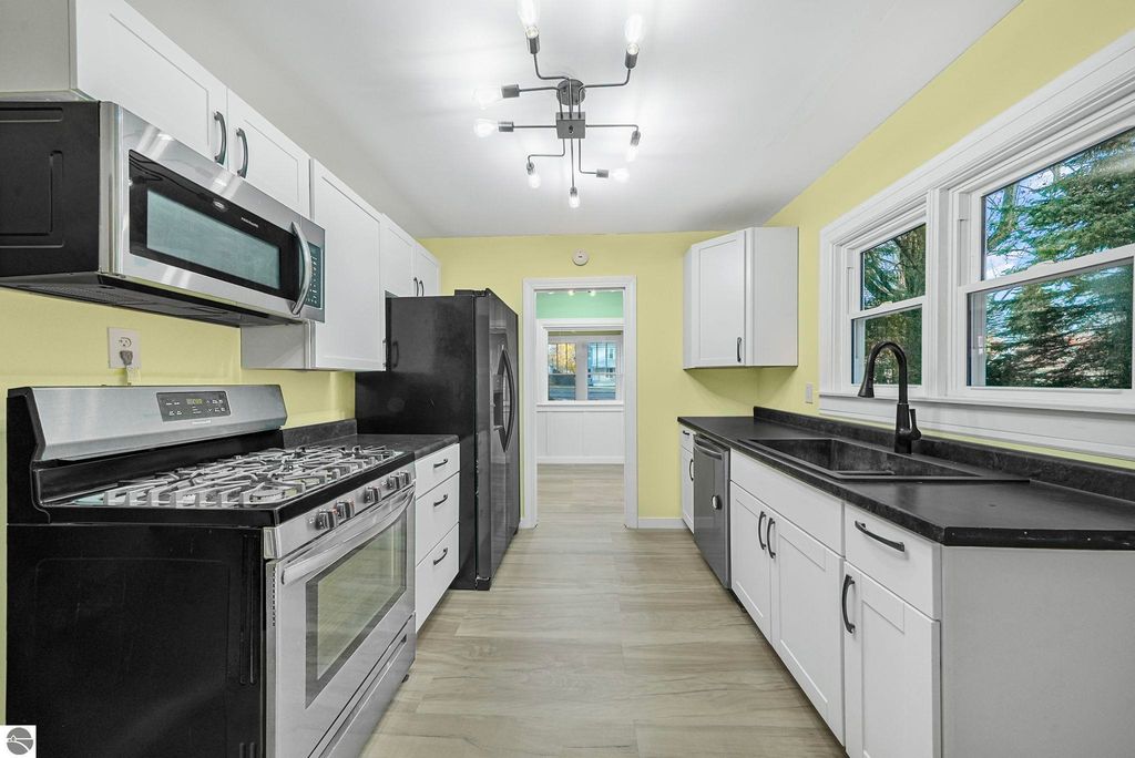 Updated kitchen with modern appliances, including stainless steel gas range, microwave, and black refrigerator, featuring white cabinetry, yellow walls, and ample natural light from windows, showcasing a stylish and functional space in the McBain home for sale at 310 E Euclid Street.