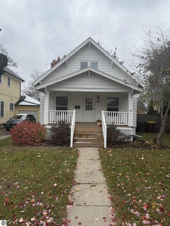 Charming white house at 610 S Washington Street, Mt Pleasant, MI, featuring a welcoming front porch, landscaped yard with autumn leaves, and nearby parked vehicles, ideal for showcasing the property&rsquo;s inviting exterior and neighborhood setting.