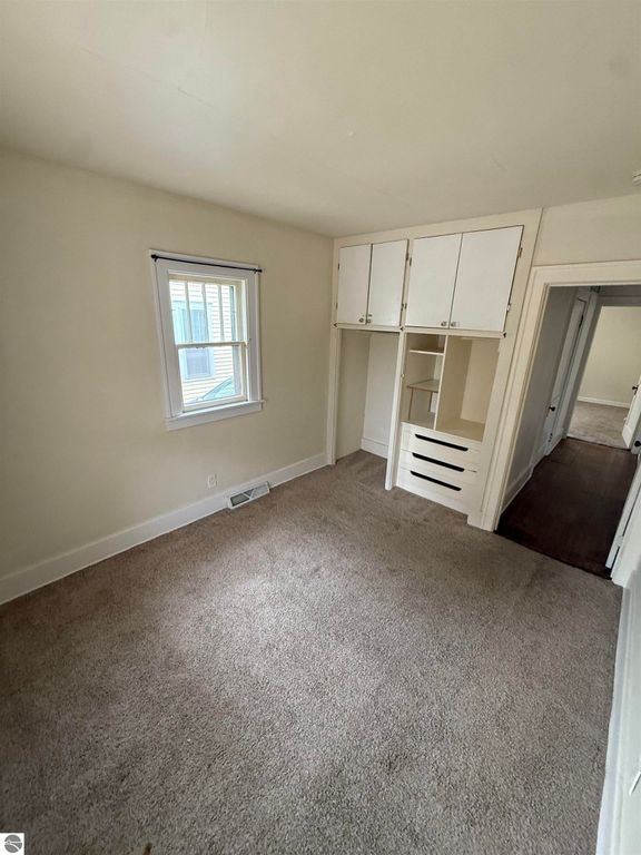 Cozy bedroom interior featuring beige carpeting, natural light from a window, and built-in storage with shelves and drawers, part of the residential listing at 610 S Washington Street, Mt Pleasant, MI.
