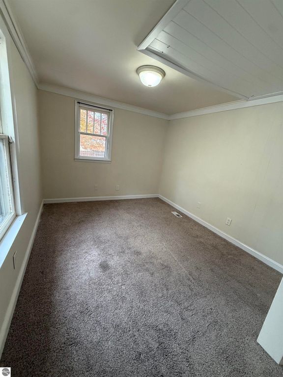 Cozy bedroom in residential property at 610 S Washington Street, featuring natural light from window, carpeted flooring, and neutral wall colors, ideal for comfortable living near downtown Mt Pleasant.