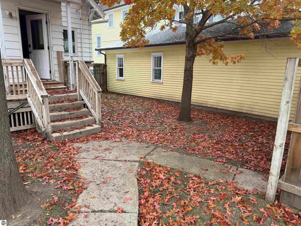 Exterior view of 610 S Washington Street, featuring a front porch with steps, a tree in the yard, and fallen leaves on the ground, highlighting the inviting atmosphere of the property in Mount Pleasant, MI.