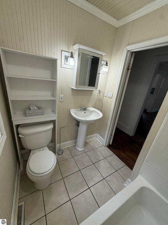 Bathroom featuring a toilet, pedestal sink, and wall-mounted mirror, with light fixtures and a built-in shelf for storage, showcasing a clean and functional design.