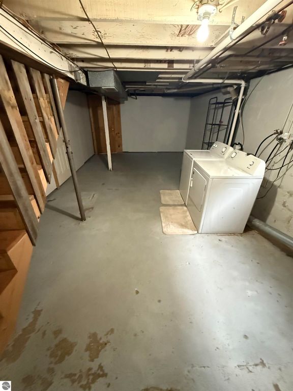Basement laundry area featuring a washer and dryer, concrete floor, and exposed beams, showcasing space for utility and storage in the home at 610 S Washington Street, Mt Pleasant, MI.