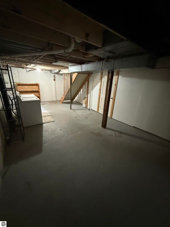 Basement interior of 610 S Washington Street, featuring exposed beams, a staircase, and laundry area, highlighting potential for additional living space or storage.