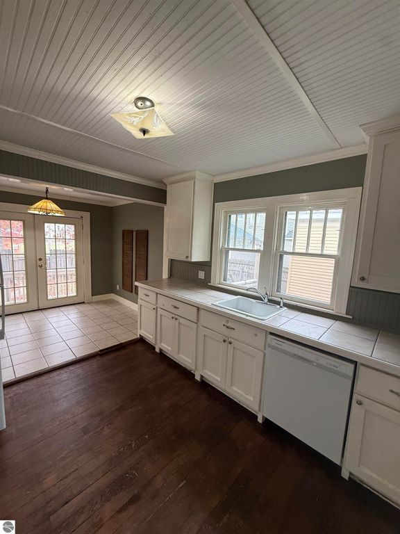 Kitchen interior of 610 S Washington St, featuring white cabinetry, a sink, and a dishwasher, with a view of a tiled floor and double doors leading to a fenced backyard.