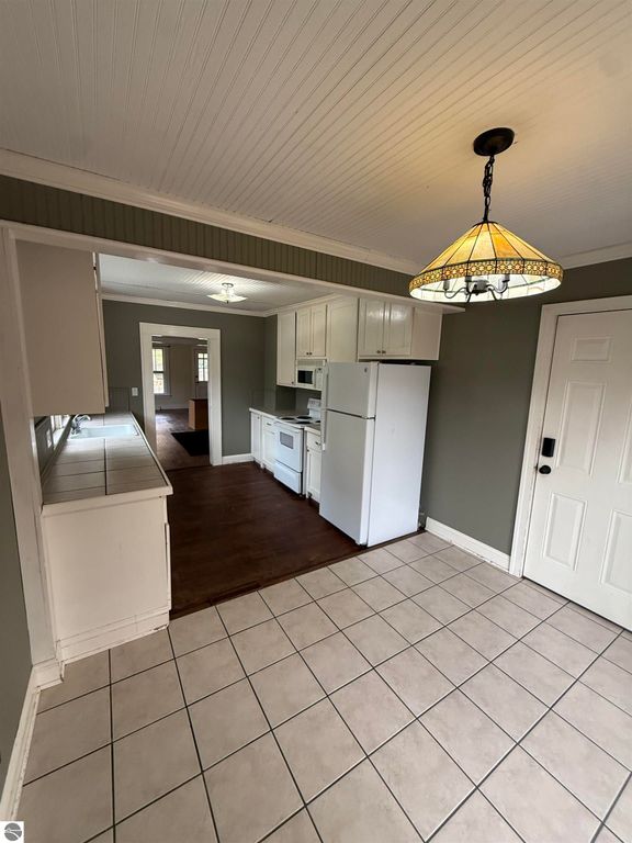 Kitchen interior of 610 S Washington Street, featuring white cabinetry, appliances, and tiled floor, with a view into the living area and a decorative ceiling light.