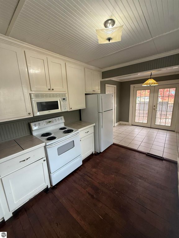 Kitchen interior of 610 S Washington Street, featuring white cabinetry, a stove, microwave, and refrigerator, with a view of the tiled area and French doors leading to a fenced backyard.