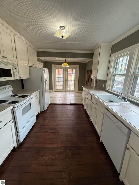 Kitchen interior featuring white cabinetry, appliances including a stove and refrigerator, and a view of a door leading to the backyard, emphasizing a warm and inviting space ideal for family living near downtown Mt Pleasant.