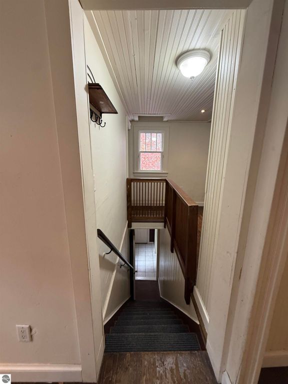 Staircase leading down to a tiled hallway with natural light from a window, showcasing the interior layout of the home at 610 S Washington Street, Mt Pleasant, MI.
