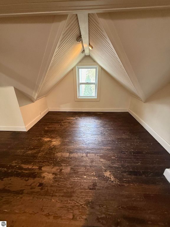 Attic room with sloped ceiling, hardwood floor, and window overlooking greenery, showcasing potential for cozy living space in the residential listing at 610 S Washington Street, Mt Pleasant, MI.