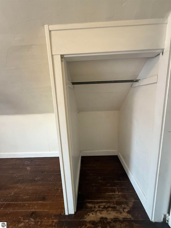 Closet space with a hanging rod in a residential property at 610 S Washington Street, Mt Pleasant, MI, featuring white walls and wooden flooring.