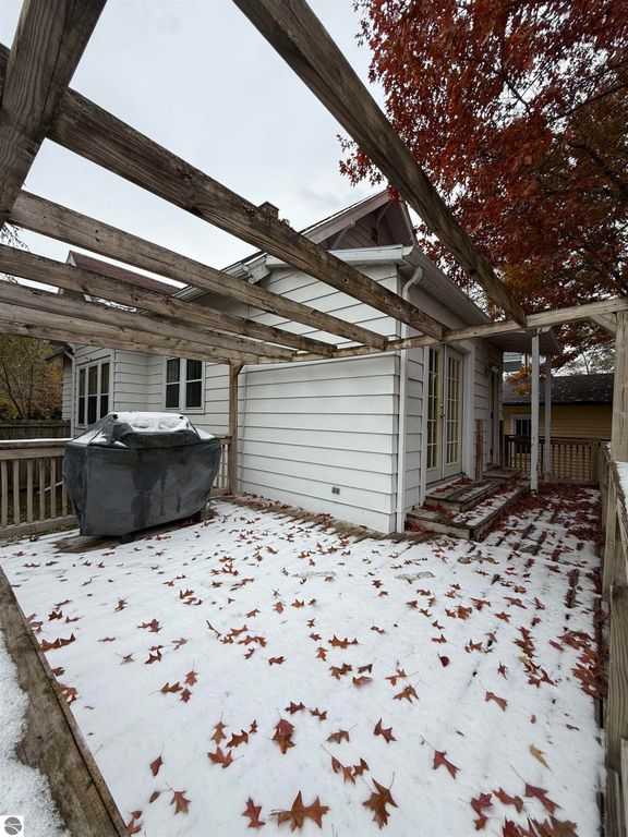 Backyard view of 610 S Washington Street, featuring a wooden pergola, snow-covered ground with fallen leaves, and a covered outdoor storage area, highlighting the property's inviting outdoor space in Mt Pleasant, MI.