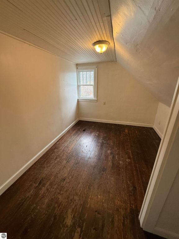 Cozy bedroom with wooden flooring, natural light from window, and sloped ceiling, part of the residential property at 610 S Washington Street, Mt Pleasant, MI.