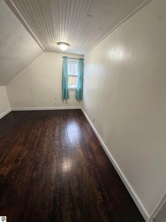 Cozy bedroom with hardwood floors, natural light from window with blue curtains, sloped ceiling, and neutral wall color in home at 610 S Washington St, Mt Pleasant, MI.