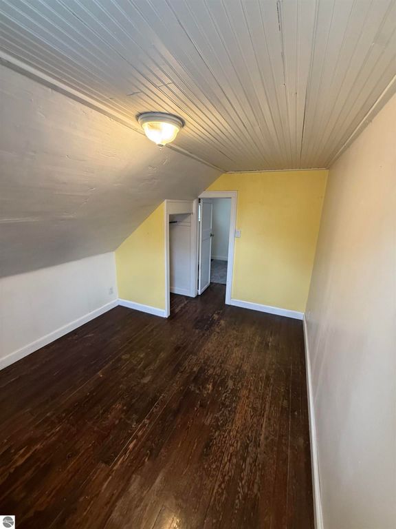 Cozy bedroom with sloped ceiling, yellow accent wall, hardwood flooring, and closet access, showcasing the inviting interior of the property at 610 S Washington Street, Mt Pleasant, MI.