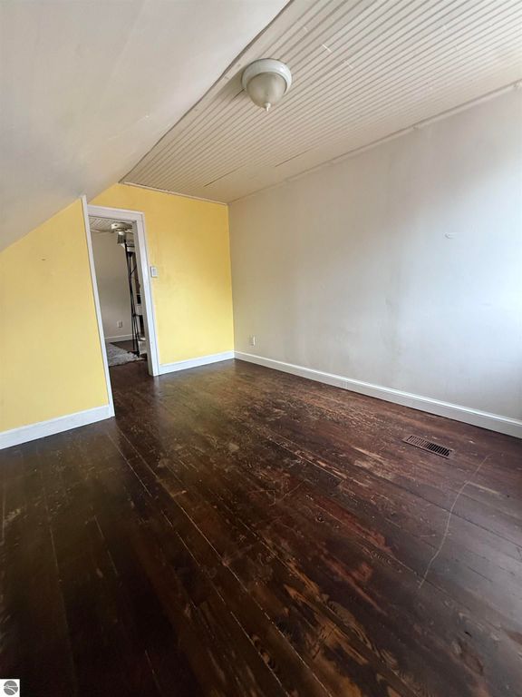 Interior view of a room in a home for sale at 610 S Washington Street, featuring yellow accent wall, hardwood flooring, and a ceiling fan, showcasing spacious layout and natural light.