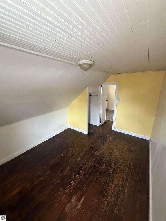 Attic bedroom with sloped ceiling, yellow walls, hardwood flooring, and doorway leading to additional room, showcasing cozy living space at 610 S Washington Street, Mt Pleasant, MI.