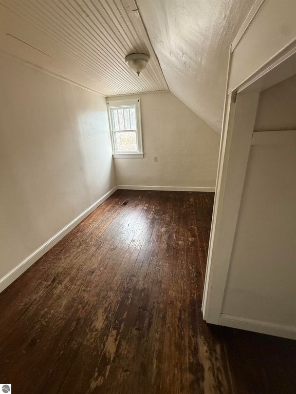Empty room with sloped ceiling, hardwood floor, and window providing natural light, showcasing interior space of the property at 610 S Washington Street, Mt Pleasant, MI.