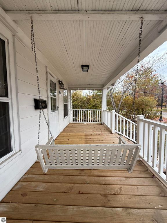 Front porch of 610 S Washington Street featuring a white swing, wooden flooring, and a welcoming entrance, highlighting the cozy outdoor space of the Mt Pleasant home for sale.