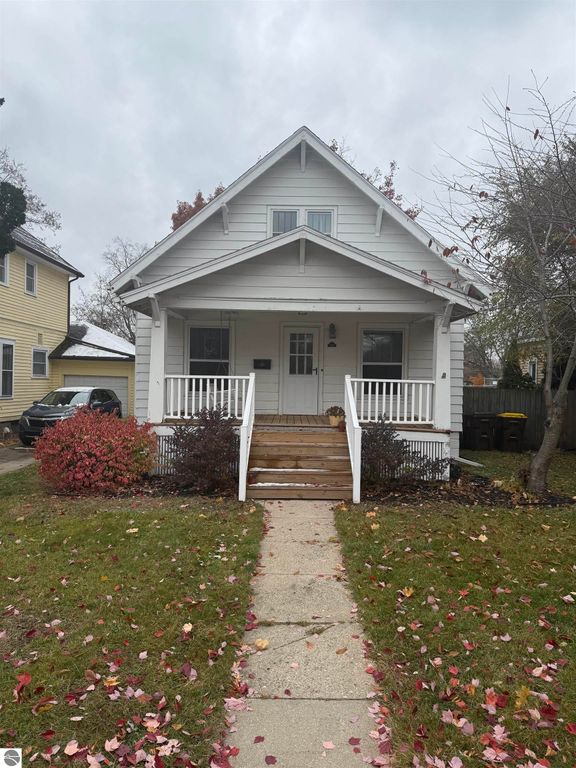 Charming white house with a welcoming porch, surrounded by colorful fall foliage, located at 610 S Washington Street, Mt Pleasant, MI, ideal for families and close to downtown amenities.
