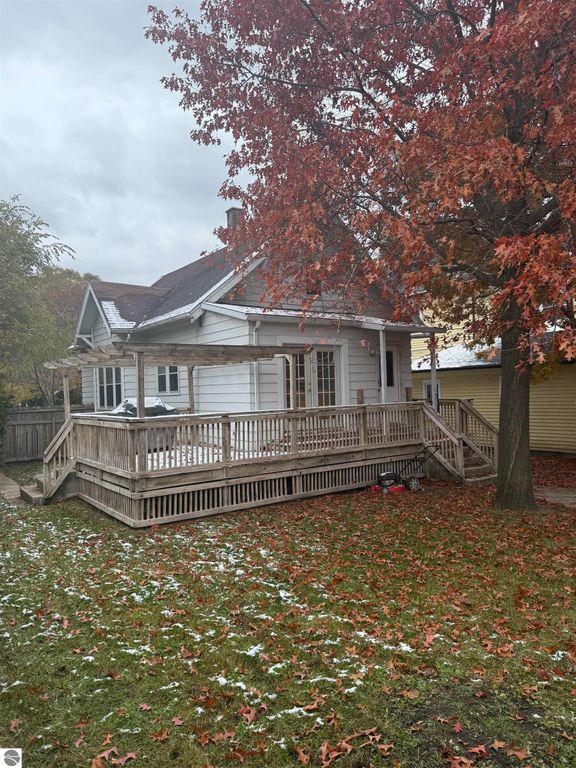 Fenced backyard of 610 S Washington Street, Mt Pleasant, with wooden deck, autumn leaves, and nearby trees, showcasing outdoor space for pets and relaxation.