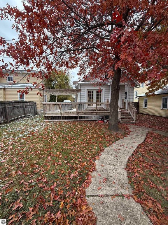 Fenced backyard of a home at 610 S Washington Street, featuring a wooden deck, colorful autumn leaves, and a pathway, highlighting the inviting outdoor space close to downtown Mount Pleasant, MI.