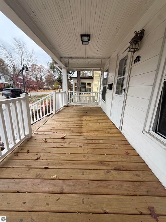 Front porch of 610 S Washington Street, featuring wooden flooring, white railings, and a welcoming entrance, with autumn leaves scattered on the ground.