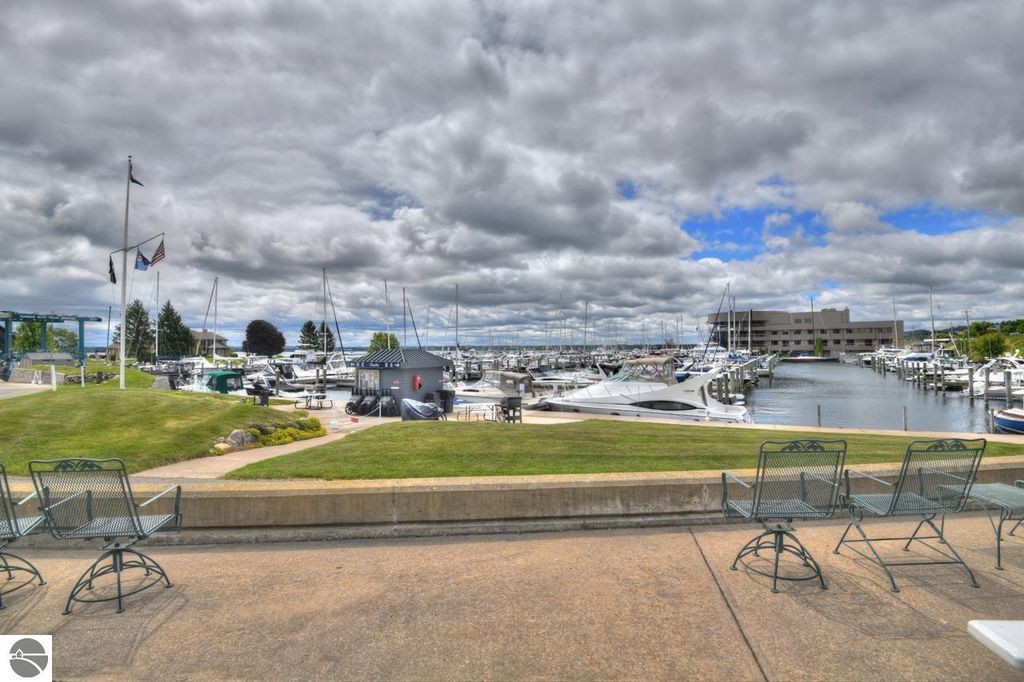 Marina view at Traverse City with multiple boats docked, grassy area with seating, and cloudy sky, highlighting the waterfront amenities near 12755 S Marina Village Drive.