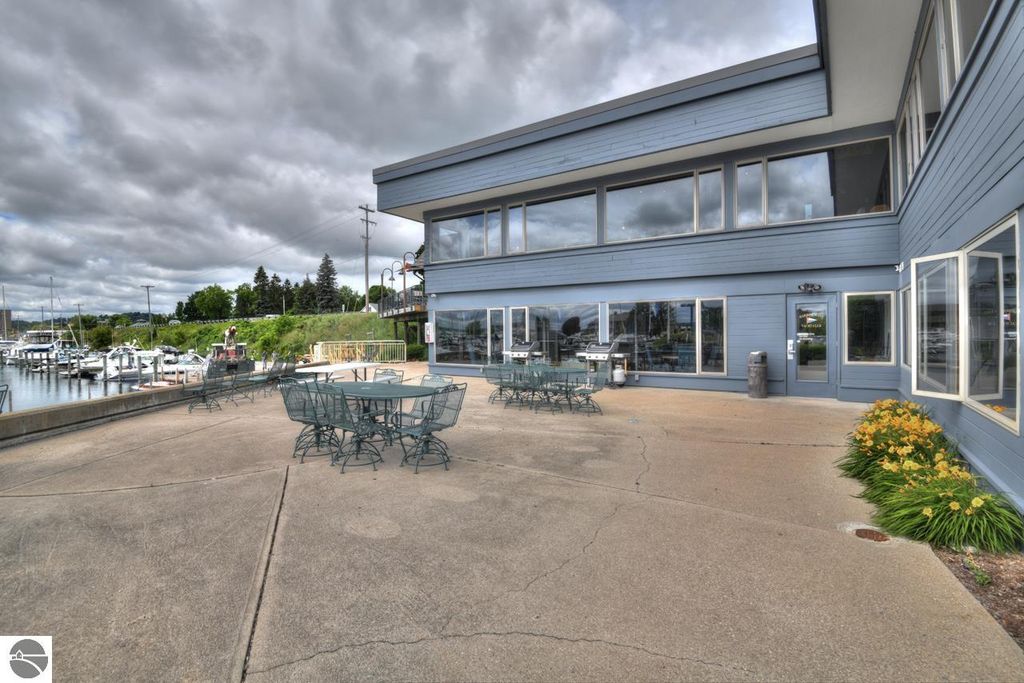 Exterior view of a marina clubhouse with outdoor seating, surrounded by boats, located in Traverse City, Michigan, near West Bay, featuring amenities for boat enthusiasts.