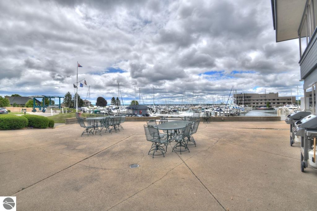Outdoor patio area with tables and chairs overlooking a marina filled with boats, featuring a cloudy sky and nearby amenities in Traverse City, Michigan.